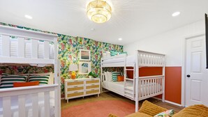 Habitación infantil con literas, cómoda y un panel decorado con motivos tropicales.