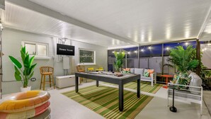 Un moderno salón con una mesa de billar, asientos cómodos y un televisor que muestra 'Home Team'.