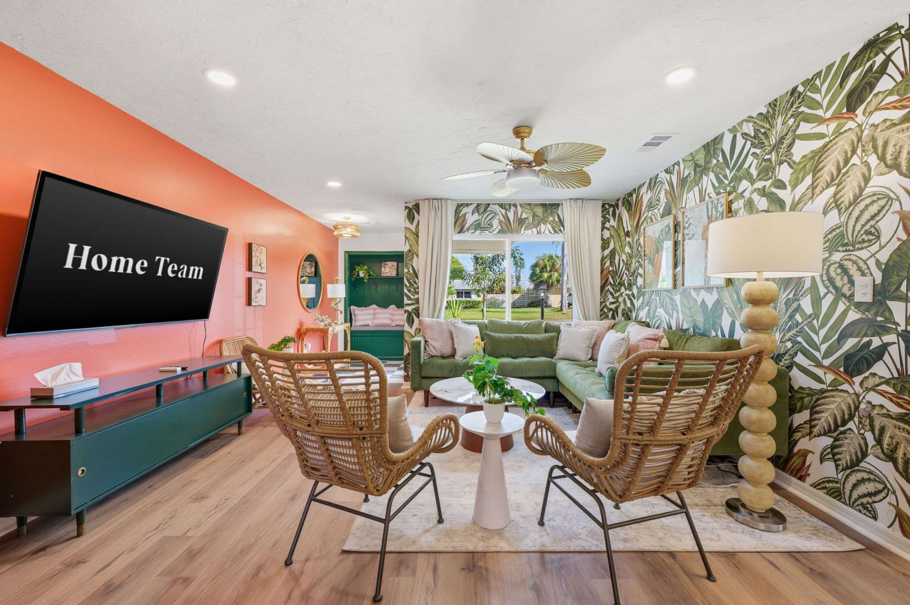 A living room with a flat-screen TV, wicker chairs, a green sofa, and a ceiling fan.