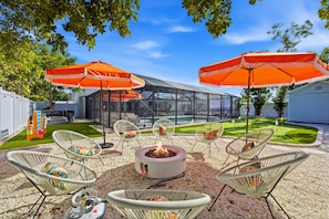 Une terrasse extérieure avec un foyer, des chaises en osier blanches et des parasols orange.