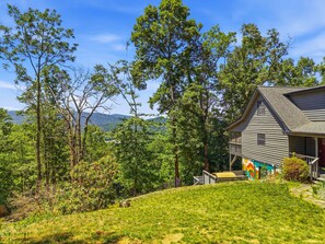 Ein Haus mit Veranda, umgeben von Bäumen und einem grasbewachsenen Hügel.
