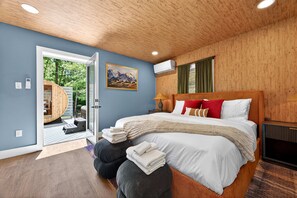 A modern bedroom with a large bed, a wooden ceiling, and a view of an outdoor sauna. - Mtn Cabin w Sauna Hot Tub Outdoor Fun (Swannanoa)