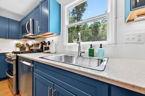 Eine moderne Küche mit blauen Schränken, einer Edelstahl-Spüle und einem Fenster mit Blick auf Grünflächen.