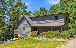 A two-story house with a sloped roof, a front porch, and a small garden area. - Mtn Cabin w Sauna Hot Tub Outdoor Fun (Swannanoa)
