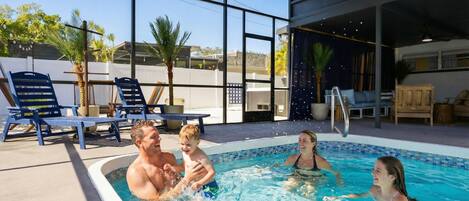A swimming pool with people enjoying the water, surrounded by lounge chairs and a covered area with seating.
