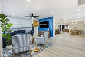 A modern living room with a sofa, armchairs, a TV, and a large window. - Breezy Livin - Speakeasy - Pool - Spa - Game Room (Bradenton)