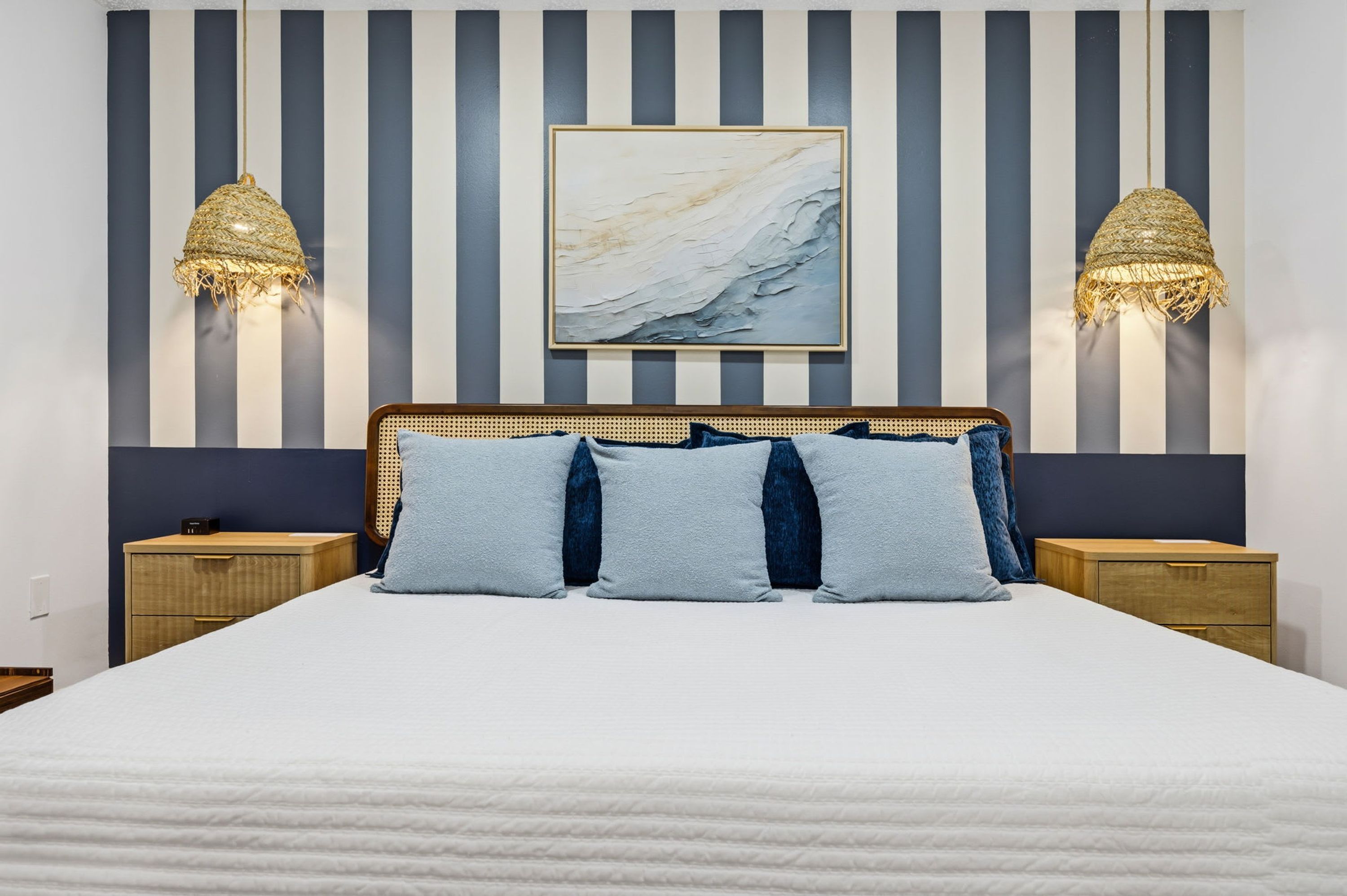 Una cama con colcha blanca, cabecera con diseño tejido y dos mesitas de noche con lámparas.