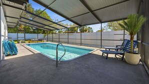 A covered outdoor swimming pool with lounge chairs and a palm tree. - Breezy Livin - Speakeasy - Pool - Spa - Game Room (Bradenton)