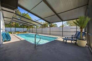 A covered outdoor swimming pool with lounge chairs and a palm tree. - Breezy Livin - Speakeasy - Pool - Spa - Game Room (Bradenton)