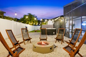An outdoor seating area with a fire pit, chairs, and a grill. - Breezy Livin - Speakeasy - Pool - Spa - Game Room (Bradenton)
