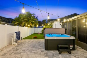 A hot tub in a backyard with a white fence, palm trees, and string lights. - Breezy Livin - Speakeasy - Pool - Spa - Game Room (Bradenton)