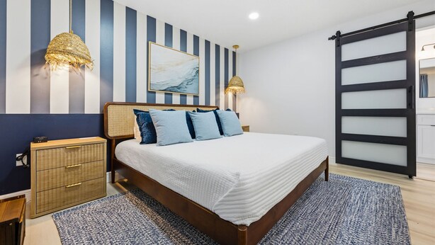 A bedroom with a bed, bedside tables, a wall-mounted artwork, and a sliding door. - Breezy Livin - Speakeasy - Pool - Spa - Game Room (Bradenton)