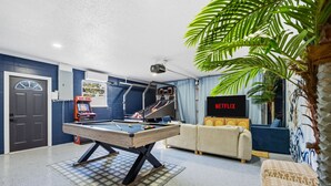 A pool table in a room with a sofa, a television, and a projector. - Breezy Livin - Speakeasy - Pool - Spa - Game Room (Bradenton)