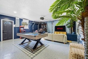 A pool table in a room with a sofa, a television, and a projector. - Breezy Livin - Speakeasy - Pool - Spa - Game Room (Bradenton)