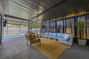 Ein überdachter Außenbereich mit Pool, einem blauen Sofagarnitur und einem Holzstuhl.