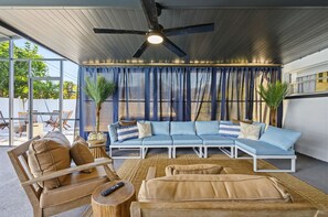 A modern living room with a sectional sofa, a wooden chair, a coffee table, and a ceiling fan. - Breezy Livin - Speakeasy - Pool - Spa - Game Room (Bradenton)