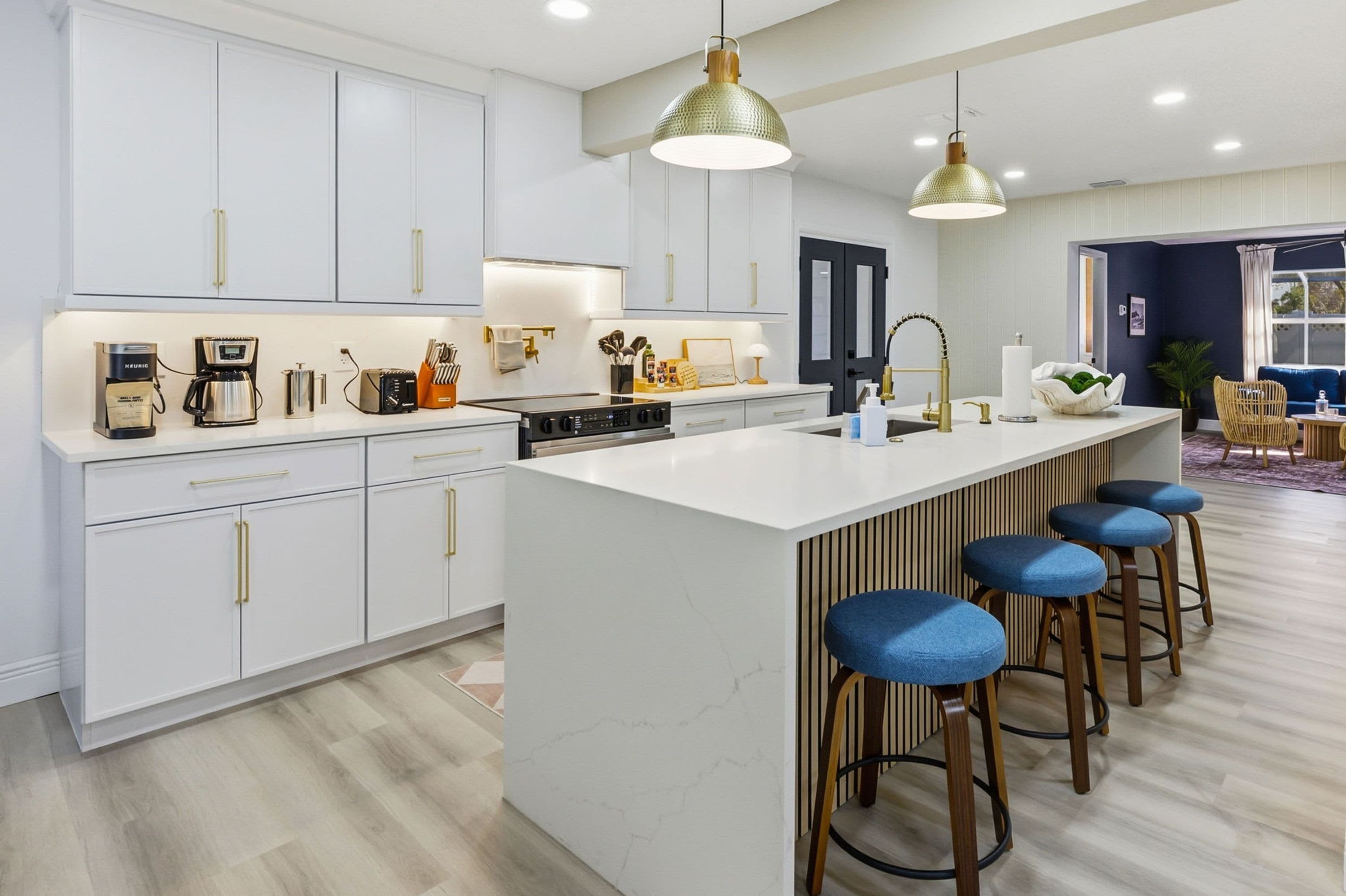 Une cuisine moderne avec des meubles blancs, un îlot central doté de tabourets et un éclairage suspendu.