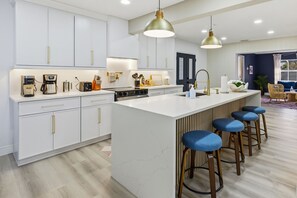 A modern kitchen with white cabinetry, a central island with bar stools, and pendant lighting. - Breezy Livin - Speakeasy - Pool - Spa - Game Room (Bradenton)