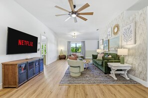 Ein modernes Wohnzimmer mit einem Flachbildfernseher, einem Deckenventilator und einem großen Fenster.