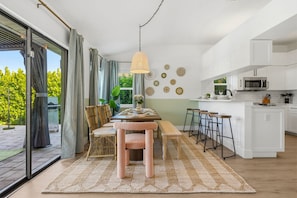 A modern kitchen with white cabinets, a central island, and a dining area with a table and chairs. - Bradenton Bliss Pool Putt Putt Arcade Games (Bradenton)