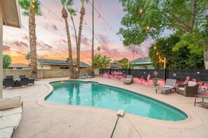 A swimming pool with lounge chairs and string lights, surrounded by palm trees and a sunset view. - The Cactus Rose Heated Pool Putterball Bocce (Glendale)