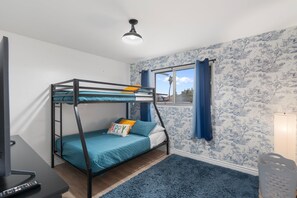Ein Stockbett mit einer Wand im blauen und weißen Muster, einem Fenster mit blauen Vorhängen und einer Deckenleuchte.