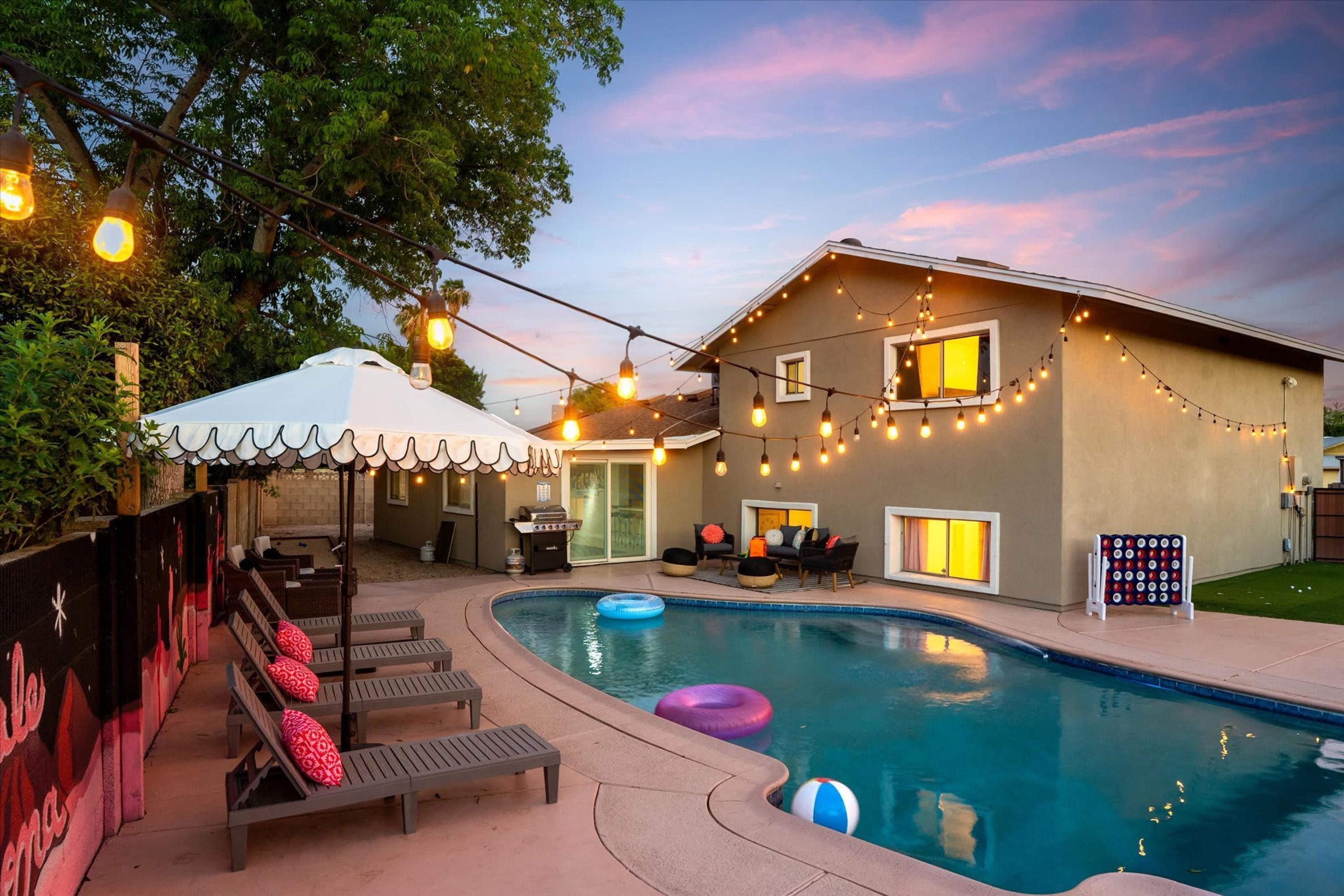 A backyard with a swimming pool, lounge chairs, and string lights.