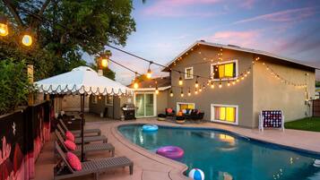 A backyard with a swimming pool, lounge chairs, and string lights.