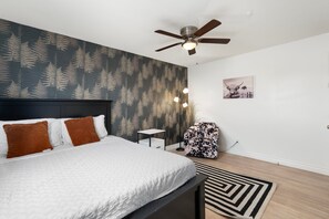 A bedroom with a bed, a ceiling fan, a small table, a chair, and a rug. - The Cactus Rose Heated Pool Putterball Bocce (Glendale)