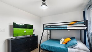 Un lit superposé avec un téléviseur posé sur une commode, un tapis bleu et une fenêtre avec des rideaux.