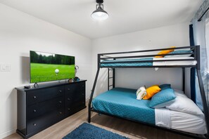 A bunk bed with a TV on a dresser, a blue rug, and a window with curtains. - The Cactus Rose Heated Pool Putterball Bocce (Glendale)