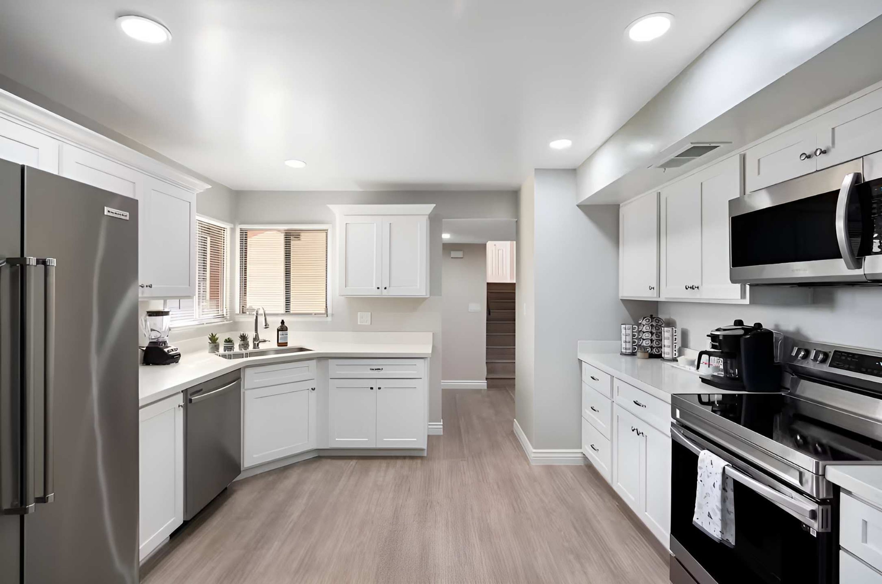 A modern kitchen with white cabinetry, a stainless steel refrigerator, an oven, and a microwave.
