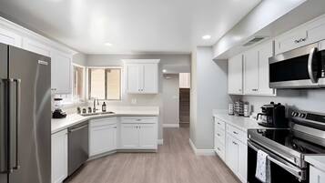 A modern kitchen with white cabinetry, a stainless steel refrigerator, an oven, and a microwave.