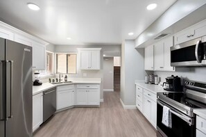 Una cocina moderna con muebles blancos, un refrigerador de acero inoxidable, un horno y un microondas.