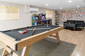 Una mesa de billar con bolas, una mesa de fútbol de mesa y una pared con un collage de fotografías.