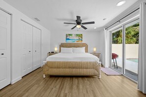 Ein Schlafzimmer mit einem großen Bett, einem Deckenventilator, einem Strandbild und Blick auf einen Pool durch eine Schiebetür.
