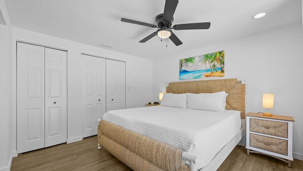 A bedroom with a bed, a ceiling fan, a painting, and a nightstand. - Sleeps 6 Private Pool Fire Pit Game House (Sarasota)