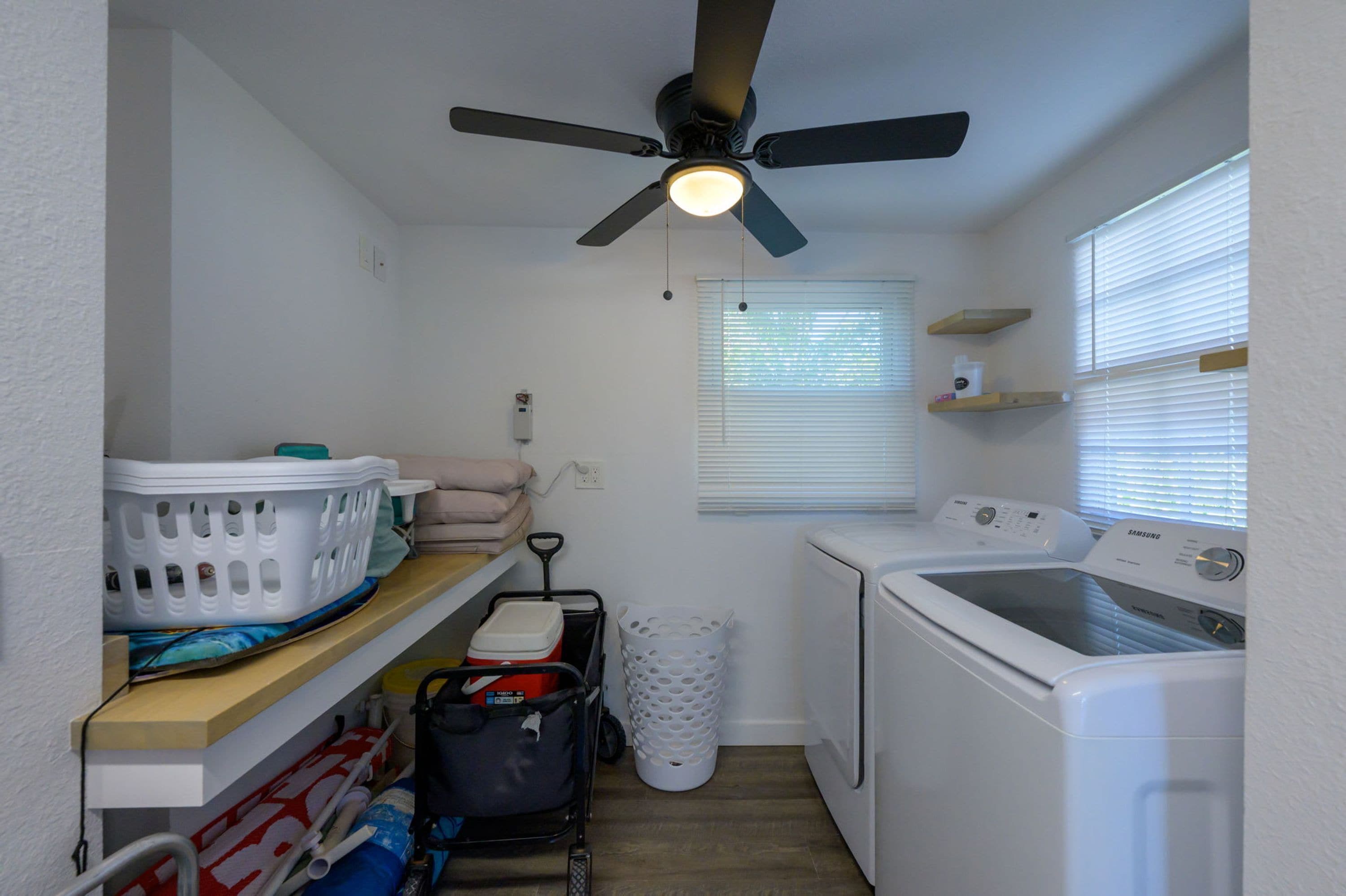 A laundry room with a ceiling fan, washing machine, dryer, and a window with blinds.