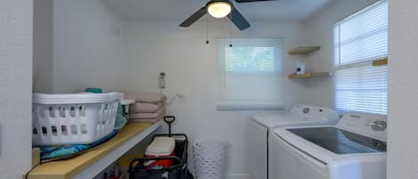 A laundry room with a ceiling fan, washing machine, dryer, and a window with blinds.