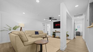A modern living room with a sofa, a coffee table, and a TV mounted on the wall. - Sleeps 6 Private Pool Fire Pit Game House (Sarasota)
