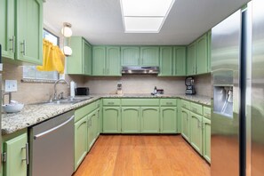 A kitchen with green cabinets, a stainless steel refrigerator, a coffee maker, and a sink. - The Texan Heated Pool Basketball Slide (San Antonio)