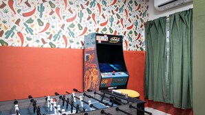 Una habitación con mesa de fútbol, máquina de videojuegos antigua y un patrón de pared colorido.