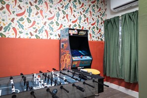 Ein Zimmer mit einem Kicker, einer Vintage-Spielmaschine und einem farbenfrohen Wandmuster.