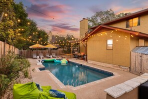 Un patio trasero con piscina, muebles de exterior, luces colgantes y valla de madera.