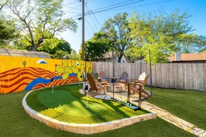 Un patio trasero con una fogata, asientos exteriores y un muro decorativo.