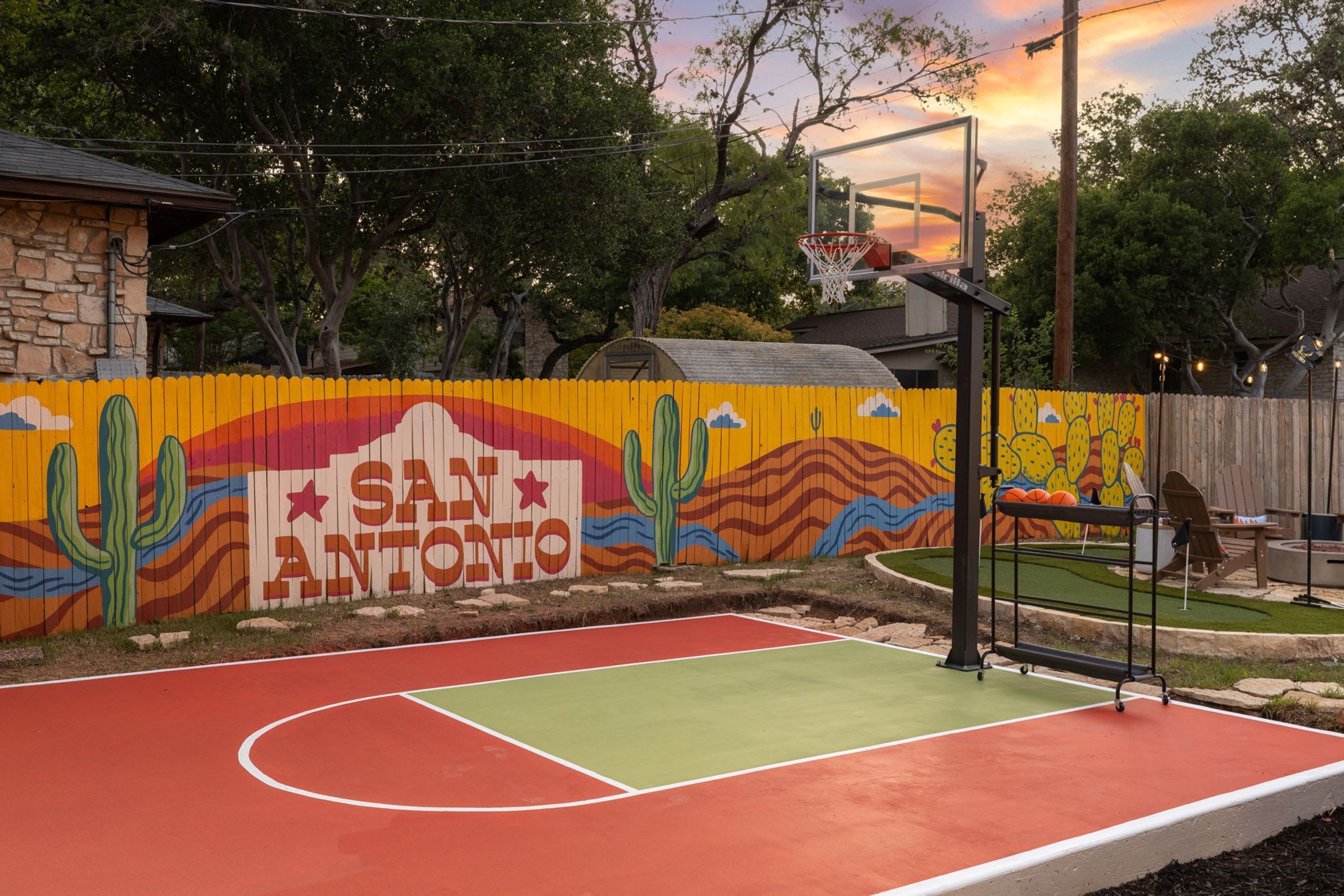 A basketball court with a mural of a desert landscape and the text 'SAN ANTONIO' on a fence.
