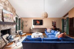 A living room with a stone fireplace, a blue sofa set, a round coffee table, and a mounted TV displaying the Netflix logo. - The Texan Heated Pool Basketball Slide (San Antonio)