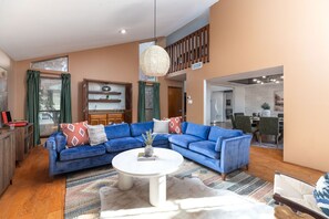 A spacious living area with a large blue sectional sofa, a white coffee table, and a dining area in the background. - The Texan Heated Pool Basketball Slide (San Antonio)