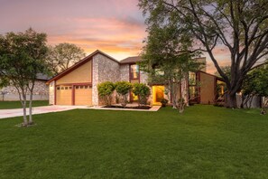 A modern two-story house with a stone facade, a garage, and a well-maintained lawn. - The Texan Heated Pool Basketball Slide (San Antonio)