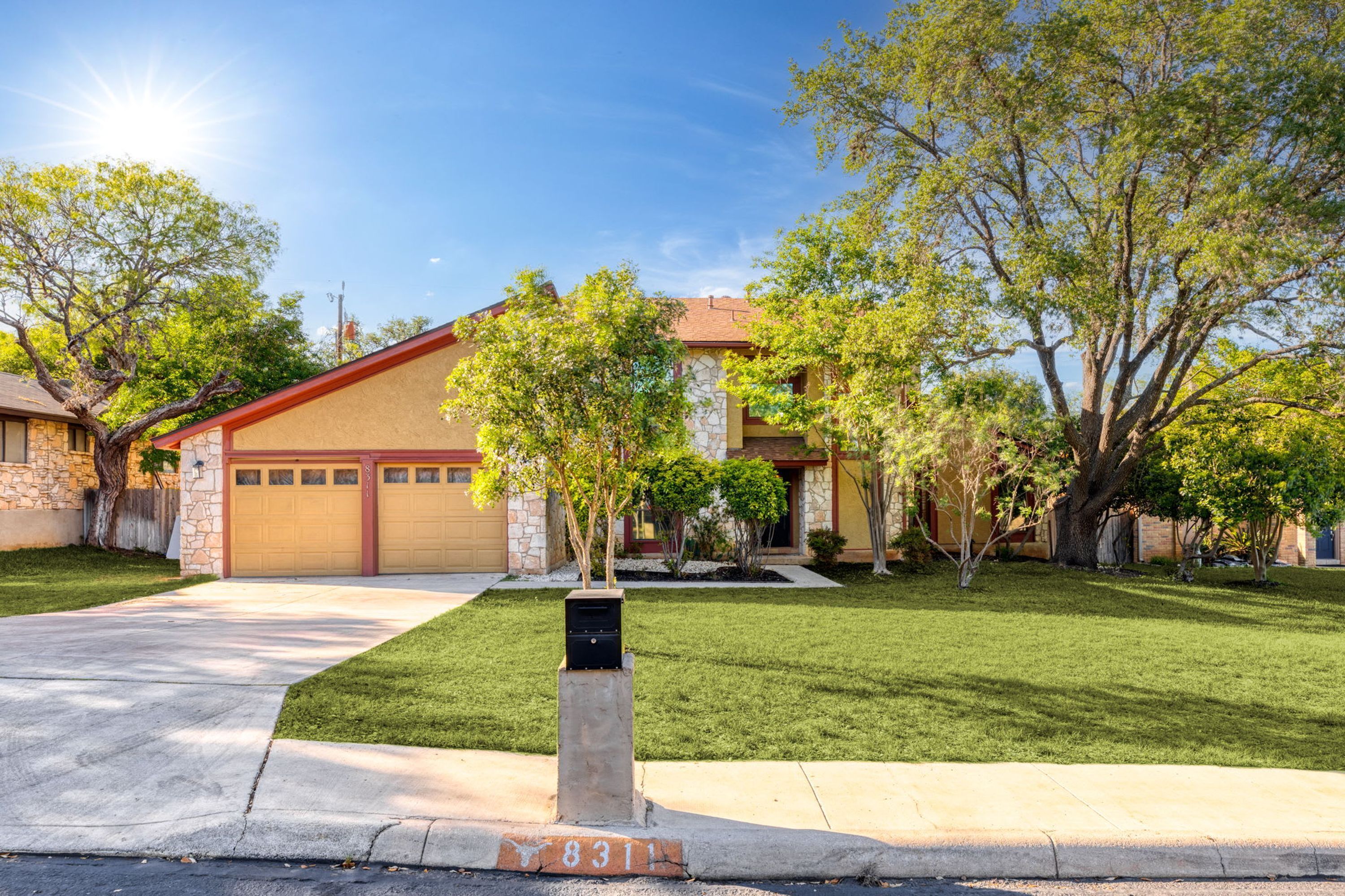 A residential house with a garage, a well-maintained lawn, and mature trees.